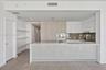Kitchen featuring a waterfall-edge quartz countertop, two-tone cabinetry with wood-finish and flat-panel white finishes, integrated appliances, and a 