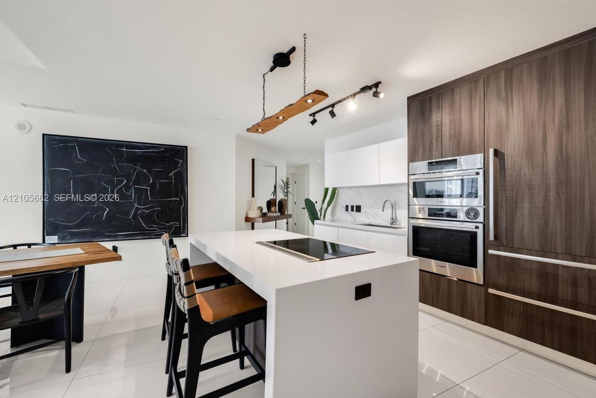 Kitchen featuring a center island with a built-in cooktop, stone-surfaced countertops, high-contrast wood-finish cabinetry, a stainless steel wall ove