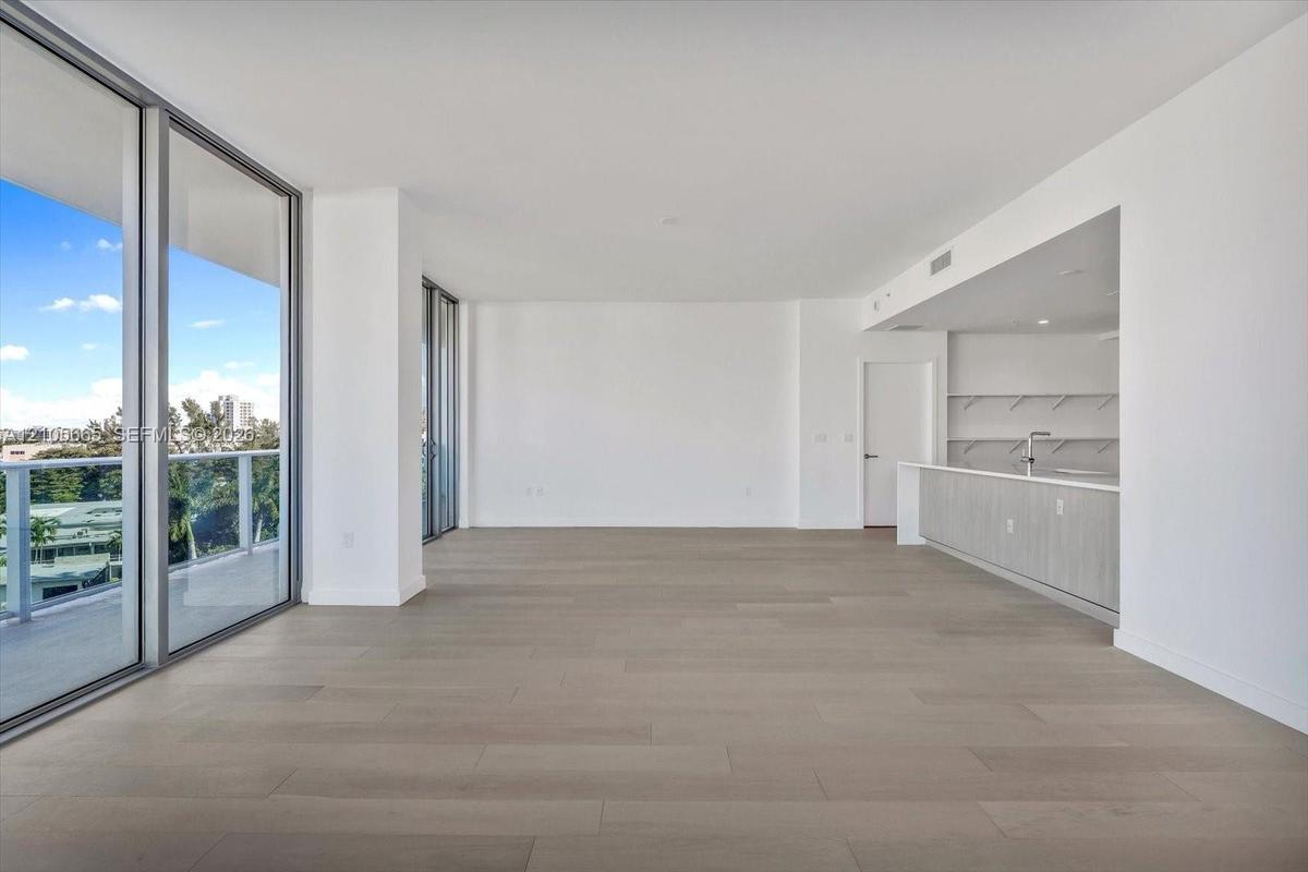 Floor-to-ceiling glass sliding doors, private balcony with metal railing, light-tone wood-finish flooring, and kitchen featuring integrated cabinetry 