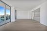 Floor-to-ceiling glass sliding doors, private balcony with metal railing, light-tone wood-finish flooring, and kitchen featuring integrated cabinetry 