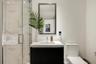 Modern vanity with a countertop basin and cabinet storage, framed wall mirror, glass-enclosed shower with large-format tile surround, and dual-flush t