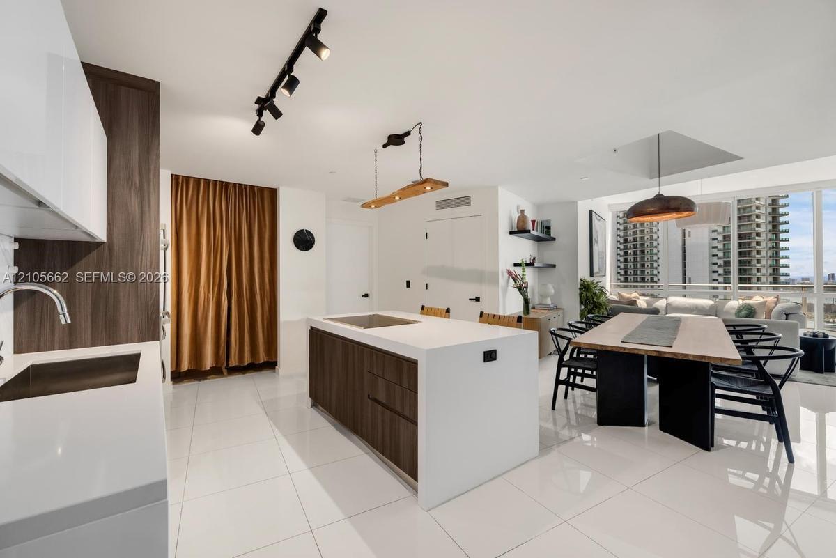 Kitchen featuring a central island with a solid-surface countertop and wood-finish cabinetry, gloss-finish white upper cabinets, track lighting, built