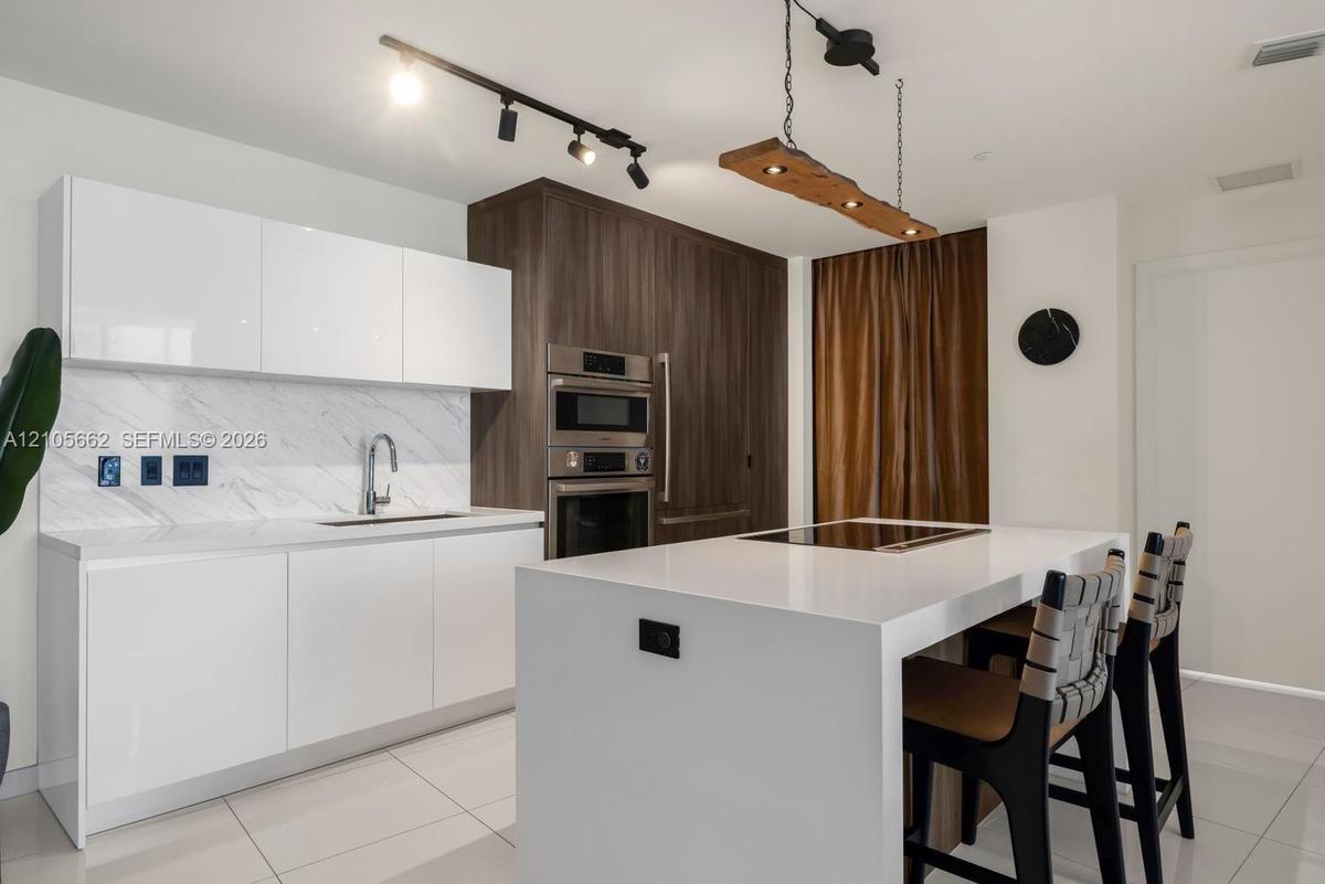 Kitchen featuring white high-gloss flat-panel cabinetry, stone-patterned backsplash, wood-finish floor-to-ceiling cabinetry with built-in stainless st