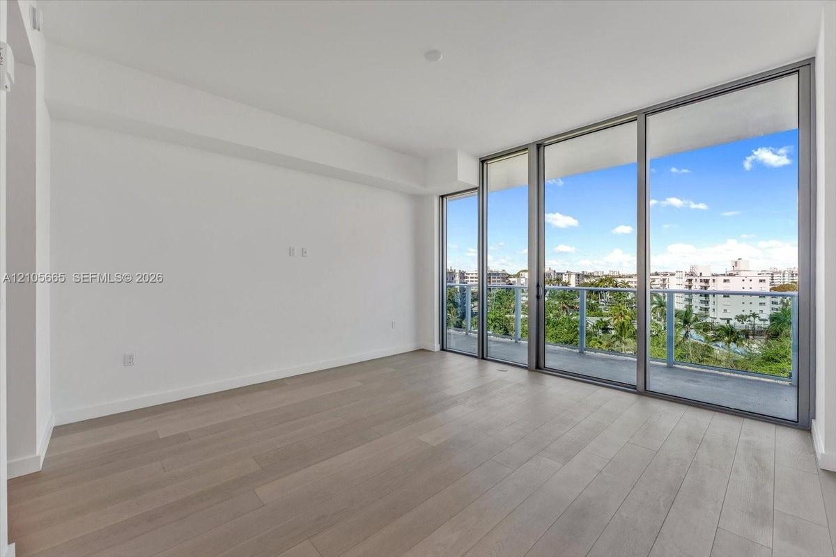 Living area featuring light-toned wood-finish flooring, floor-to-ceiling glass panels, and an outdoor balcony with metal railings