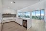 Contemporary kitchen featuring white flat-panel cabinetry, a stone-surfaced island with an integrated wine cooler, wood-finish flooring, and floor-to-