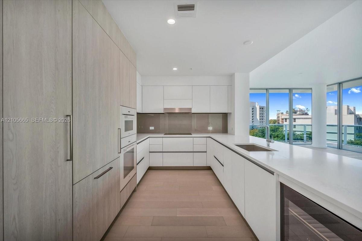Kitchen featuring flat-panel cabinetry, quartz countertops, integrated stainless steel appliances, a glass backsplash, and wood-finish flooring