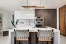 Kitchen featuring a waterfall-edge center island, built-in stainless steel double oven, custom wood-finish cabinetry, natural stone-patterned backspla