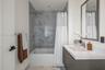 Wall-mounted floating vanity with integrated rectangular sink and solid surface countertop, mirror with framed border, and bathtub featuring patterned