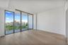 Floor-to-ceiling windows, wood-finish flooring, and a glass-railed balcony with exterior urban scenery