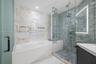 Bathroom featuring a deep soaking tub, walk-in glass-enclosed shower with a built-in bench, textured stone tile wall accents, and an integrated LED-ba