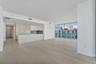 Open-concept interior featuring light-toned wood-finish flooring, floor-to-ceiling glass paneling, and a kitchen equipped with a large island, flat-pa