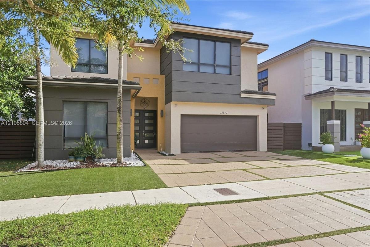 Contemporary exterior featuring two-tone stucco siding, a multi-pane glass entry door, expansive windows, and a paved driveway with integrated turf st