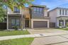 Contemporary exterior featuring two-tone stucco siding, a multi-pane glass entry door, expansive windows, and a paved driveway with integrated turf st