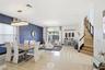Open-concept interior featuring oversized tile flooring, a blue textured accent wall, dual crystal chandeliers, and a staircase with wood-tread stairs