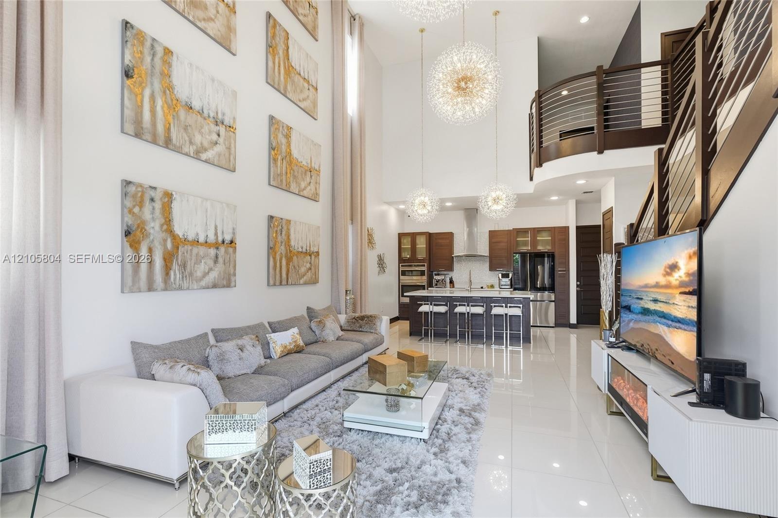 Double-height ceilings, porcelain tile flooring, kitchen featuring custom wood cabinetry and stainless steel appliances, tiered pendant lighting, and 