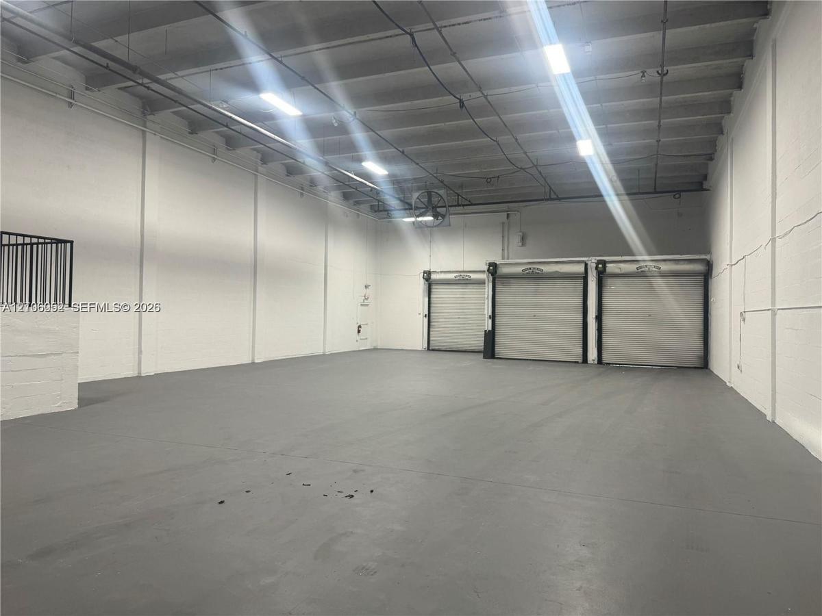Industrial warehouse space featuring high ceilings, painted masonry walls, sealed concrete flooring, three metal roll-up doors, and overhead lighting