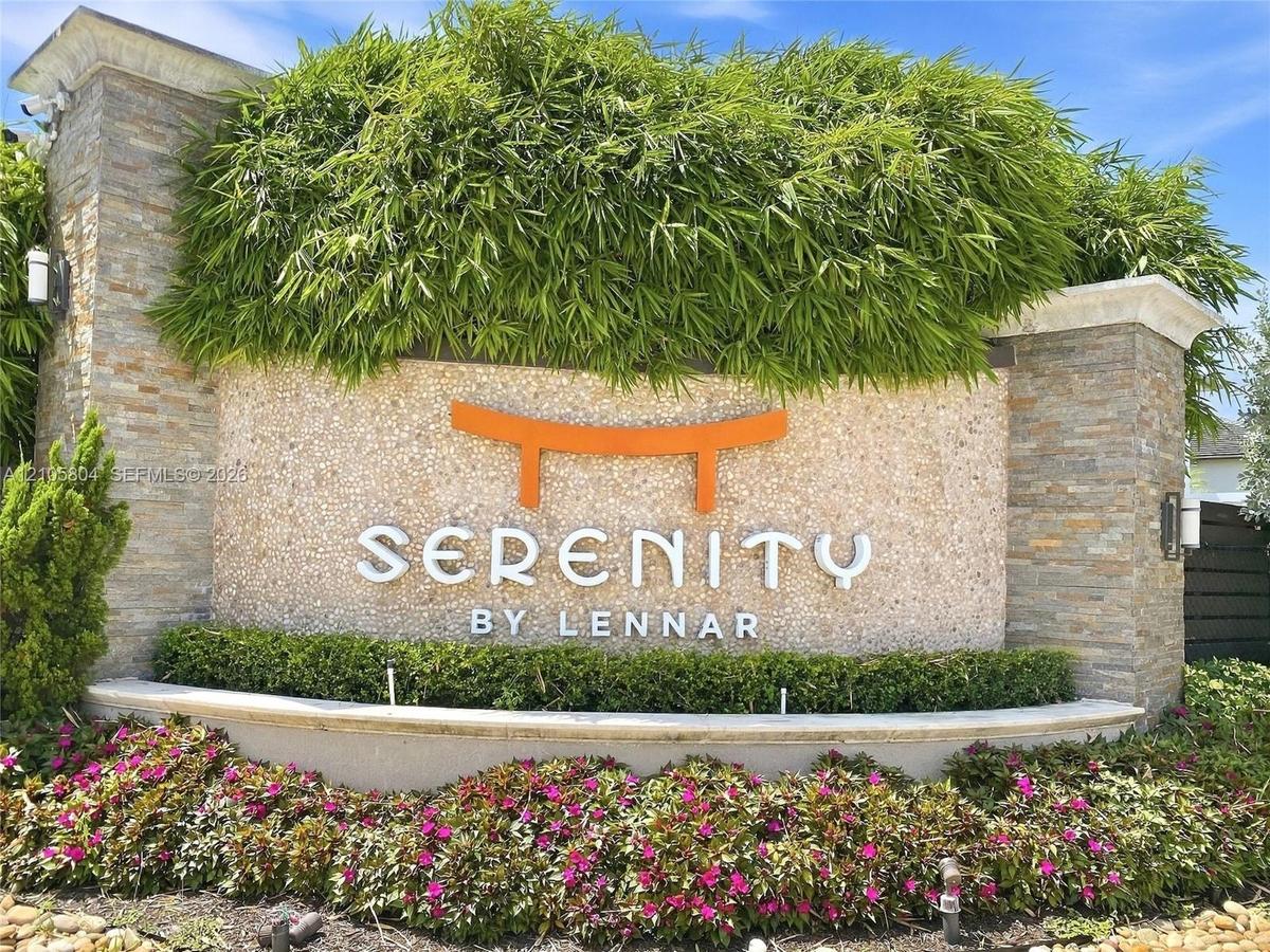 Community entrance sign featuring stacked stone columns, textured masonry, tiered landscaping, and metal accent lighting