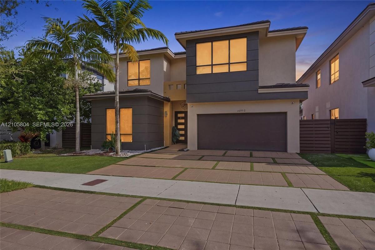 Modern two-story residence featuring a two-tone stucco facade, oversized paver driveway with integrated turf ribbons, multi-pane casement windows, and