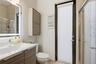 Bathroom featuring a vanity with integrated sink, wood-finish cabinetry, a backlit mirror, a wall-mounted storage cabinet, and a glass-enclosed shower