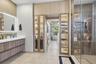 Floating vanity with stone countertop and backlit mirror, floor-to-ceiling built-in cabinetry featuring glass-front display panels, and a walk-in show