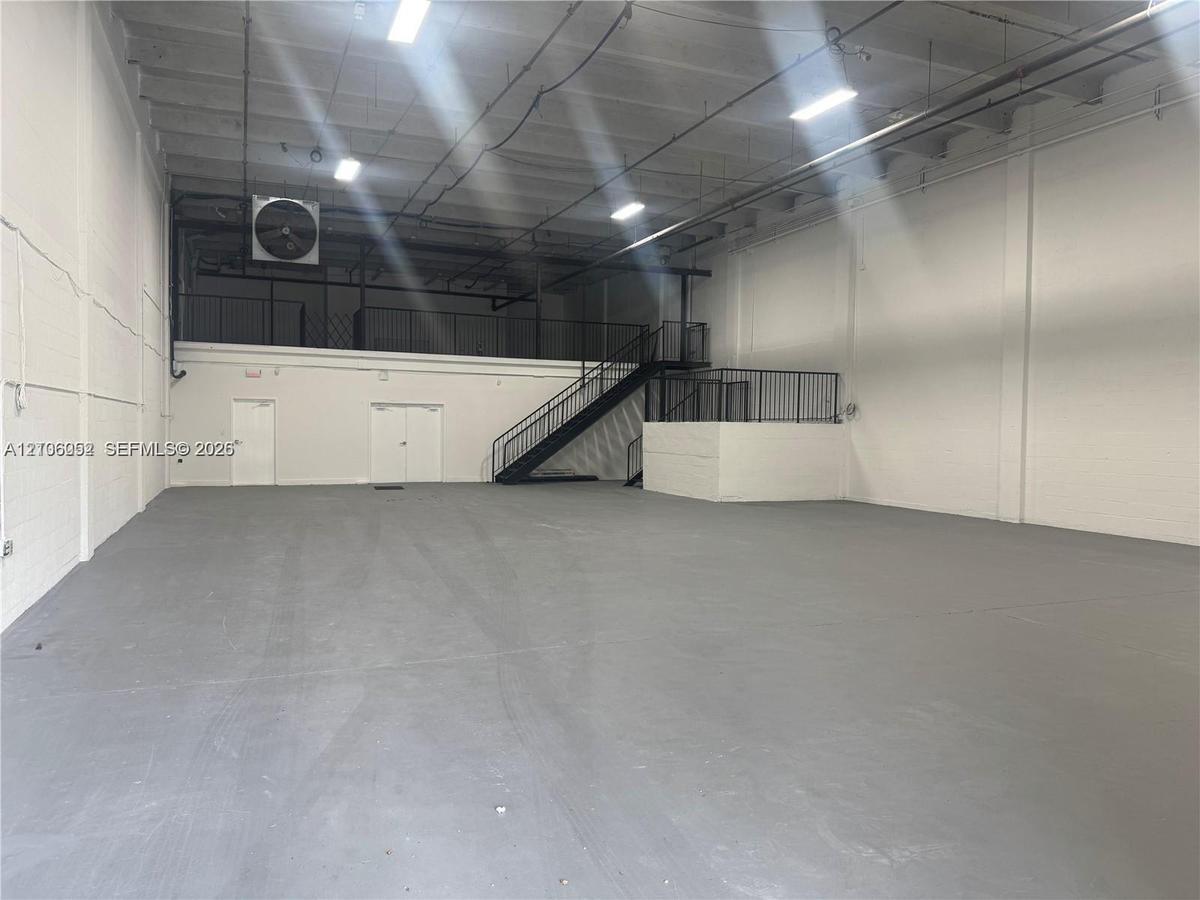 Open-concept industrial warehouse space featuring high ceilings, painted masonry walls, durable floor surfacing, mezzanine level with metal railing, a