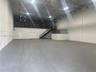 Open-concept industrial warehouse space featuring high ceilings, painted masonry walls, durable floor surfacing, mezzanine level with metal railing, a