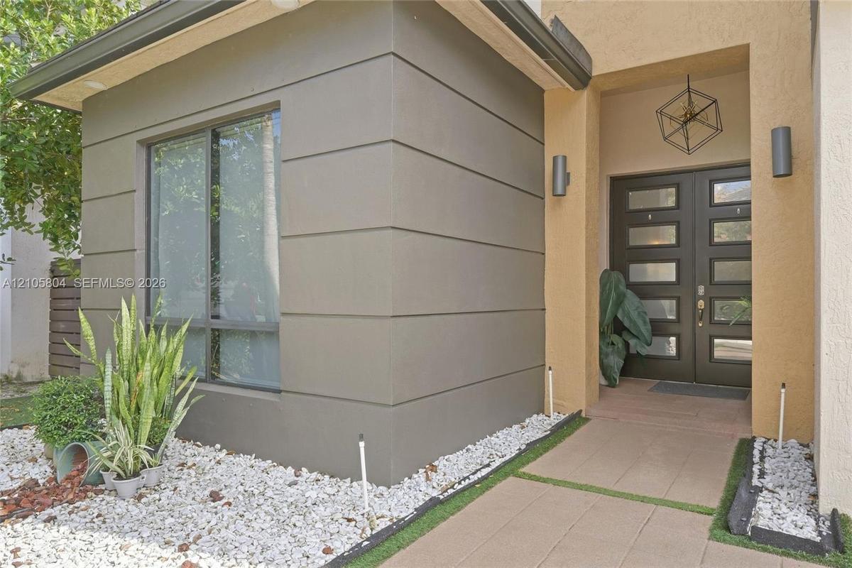 Modern exterior facade featuring smooth stucco finishes, horizontal architectural detailing, double-entry door with glass panels, geometric metal pend