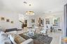 Open-concept living space featuring high-gloss tile flooring, dual tiered crystal chandelier fixtures, and a glass-paneled staircase railing