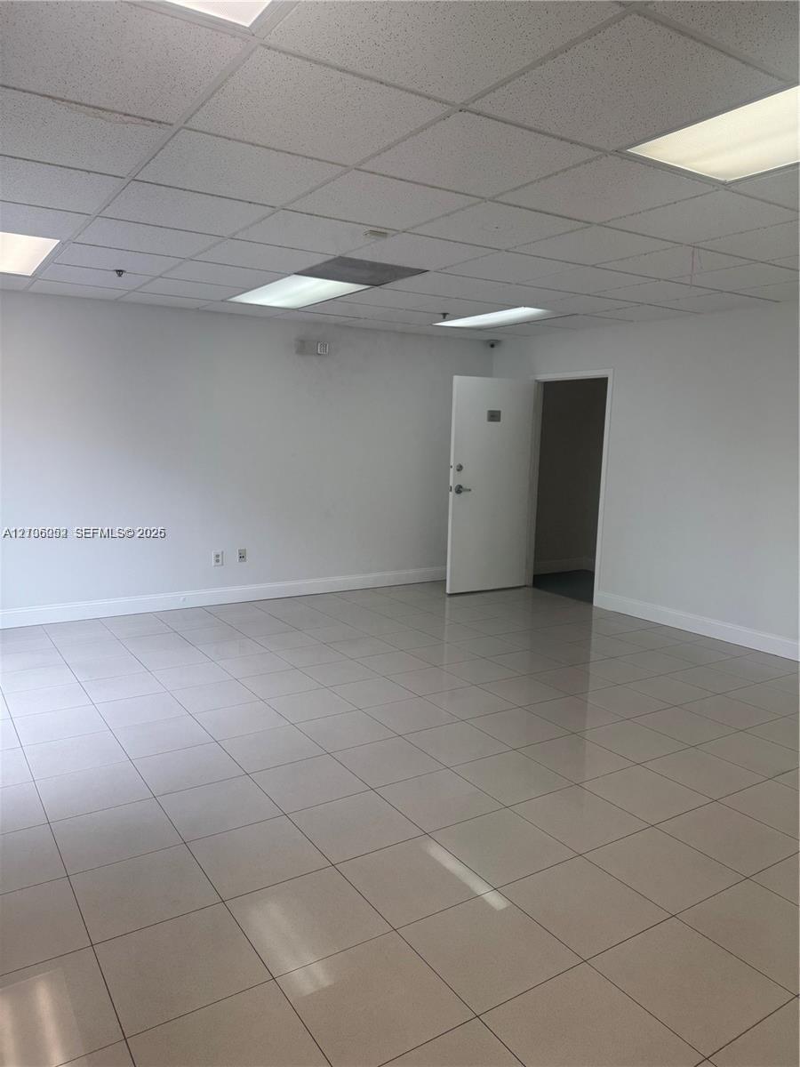 Open interior space featuring light-toned tile flooring, a drop ceiling, recessed panel lighting, and a single hinged door