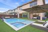Stucco exterior featuring a pool with an integrated spa, stone-finished coping, artificial turf hardscaping, and a decorative exterior wall panel