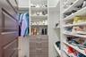 Custom walk-in closet featuring extensive built-in white shelving, integrated wood-finish cabinetry with silver-toned hardware, and a metal clothing r