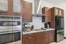 Kitchen featuring wood-finish cabinetry, stone-surface countertops, textured tile backsplash, stainless steel double wall ovens, and a stainless steel