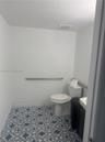 Bathroom featuring patterned floor tile, elongated toilet, and wall-mounted metal grab bars