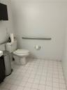 Restroom featuring white ceramic floor tiling, a porcelain toilet, and a mounted stainless steel grab bar