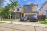 Contemporary two-story exterior featuring a multi-toned stucco facade, paver driveway with turf accents, mature palm trees, and an attached two-car ga