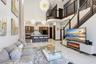 Double-height ceilings featuring tiered spherical pendant lighting, polished stone-finish flooring, and a curved staircase with dark-stained wood hand