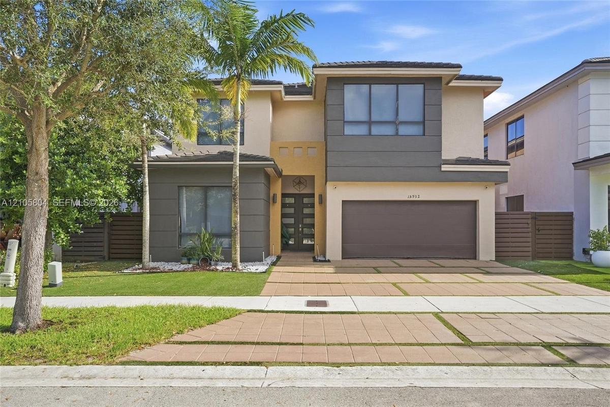Two-story contemporary exterior featuring a multi-tonal facade, recessed entryway with multi-panel double doors, two-car garage, and geometric paver d