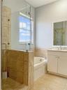 Bathroom featuring a glass-enclosed shower with stone-finish wall tile, a deep soaking tub, and a white vanity with a polished metal faucet