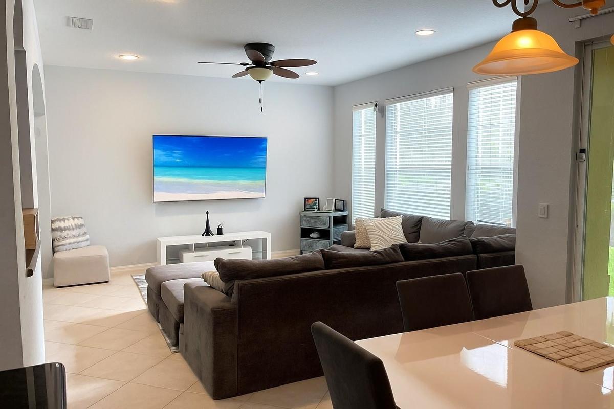 Living area featuring neutral tile flooring, recessed ceiling lighting, a multi-blade ceiling fan, and three large windows with horizontal blinds
