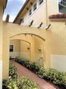 Stucco exterior featuring dual arched walkways, exposed timber rafters, and a brick-paved path bordered by mature shrubbery