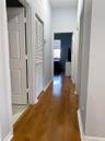 Hallway featuring wood-finish flooring, white paneled doors, and louvered closet doors