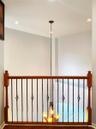 Interior railing featuring wood handrails, wood newel posts, and decorative metal balusters, accented by a multi-light pendant fixture with a chain su