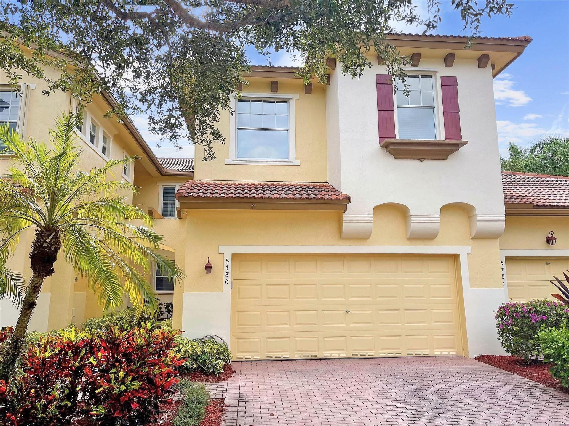 Stucco exterior featuring decorative corbels, a paver driveway, tiled roof accents, and window shutters