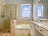 Bathroom featuring a glass-enclosed walk-in shower with stone tile surround, a built-in soaking tub, a single-sink vanity with countertop, and a frame