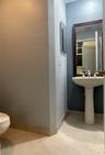 Pedestal sink featuring a polished chrome faucet, wall-mounted dark wood-frame mirror, and neutral-tone tile flooring