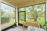 Screened-in patio featuring floor-to-ceiling window panels, black metal framing, a dedicated screen door, concrete flooring, and water frontage
