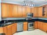 Kitchen featuring wood cabinetry, stone countertops, stainless steel appliances, and a linear open-frame pendant light fixture
