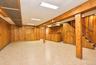 Interior space featuring wood-panelled walls, ceramic tile flooring, a built-in wooden bar, an open wooden staircase, and exposed structural support p