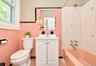 1st. Floor: Bathroom featuring pink square wall tiles with black trim, a white vanity cabinet with an integrated basin, a porcelain soaking tub, and a