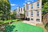 Exterior featuring a multi-story masonry facade, an elevated wooden deck, a concrete rear patio, and metal bulk-head cellar doors